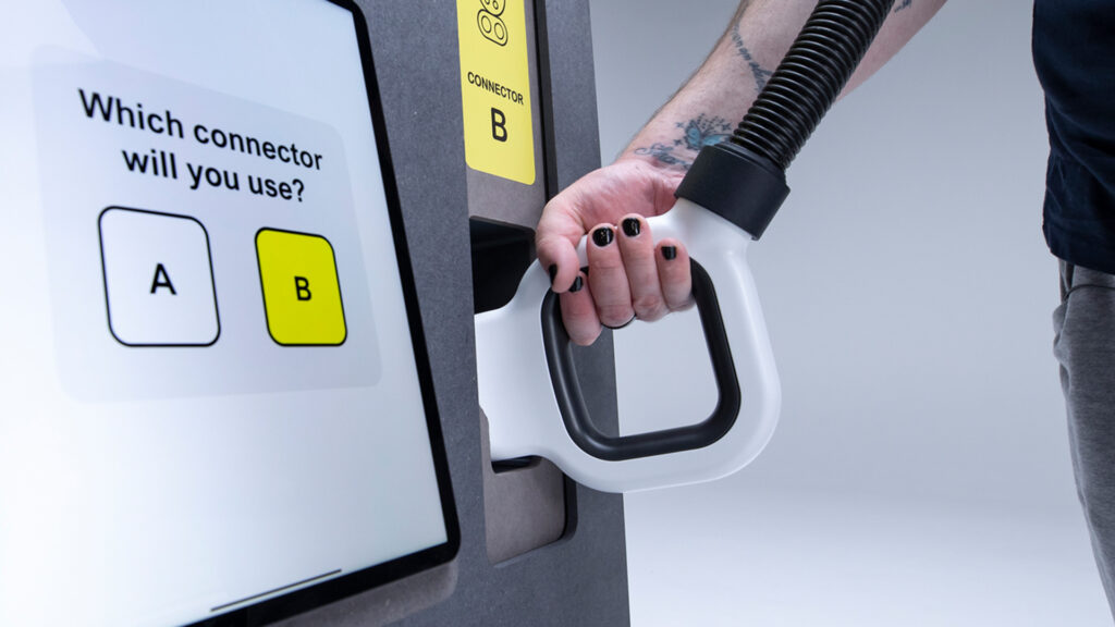 Close up photo of a hand holding the top of the square looped connector attached to a rapid charging unit’s tethered cable, as it sits in the holder on the front of the rapid charging unit.